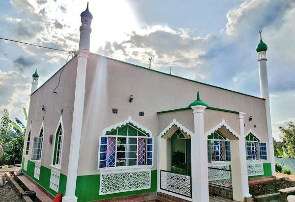 Newly constructed mosque with green and white exterior, decorative windows, and minarets under a bright sky