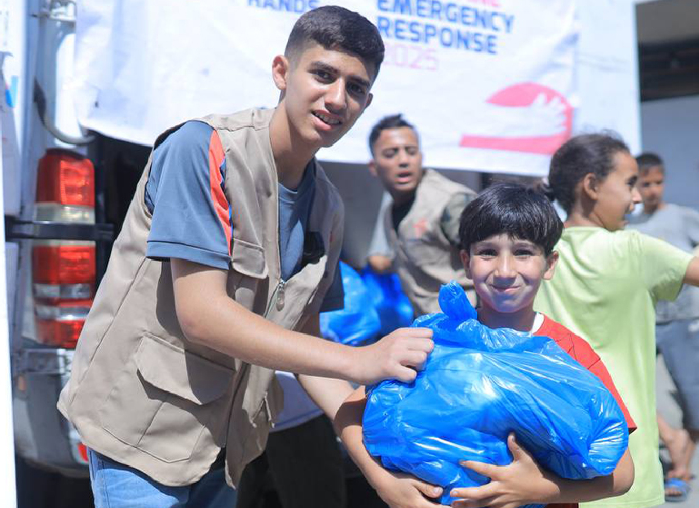 A Giving Hands volunteer hands a large blue aid package to a child during a community distribution event.