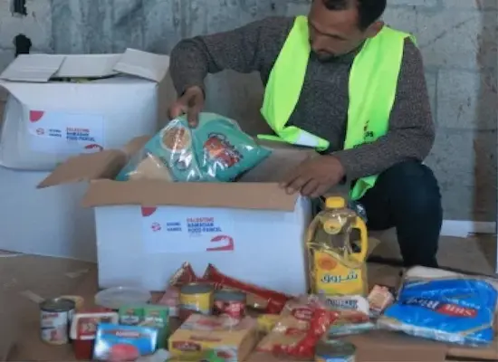 A Giving Hands volunteer organizes food items and supplies into boxes for distribution.