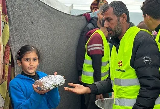 A volunteer in a Giving Hands vest hands a wrapped meal to a child during a food distribution event.