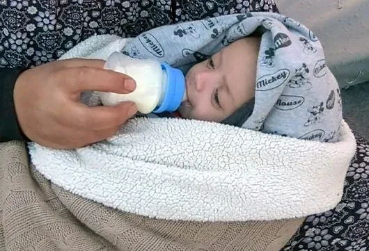 A caregiver feeds a swaddled infant with a bottle, providing essential nutrition and comfort.