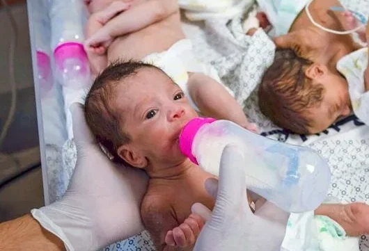 A healthcare worker wearing gloves feeds a newborn baby with a bottle in a medical setting.