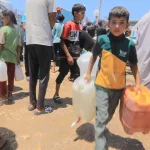 Children and adults carry water containers in a crowded outdoor setting during a Giving Hands humanitarian aid distribution.
