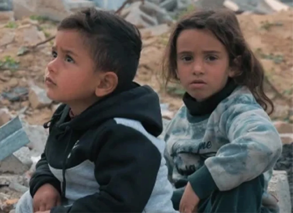 Two children sit among rubble and debris, supported by Giving Hands’ humanitarian relief efforts.