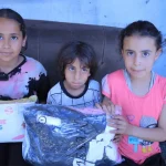 Three children sit on a couch holding packages labeled 
