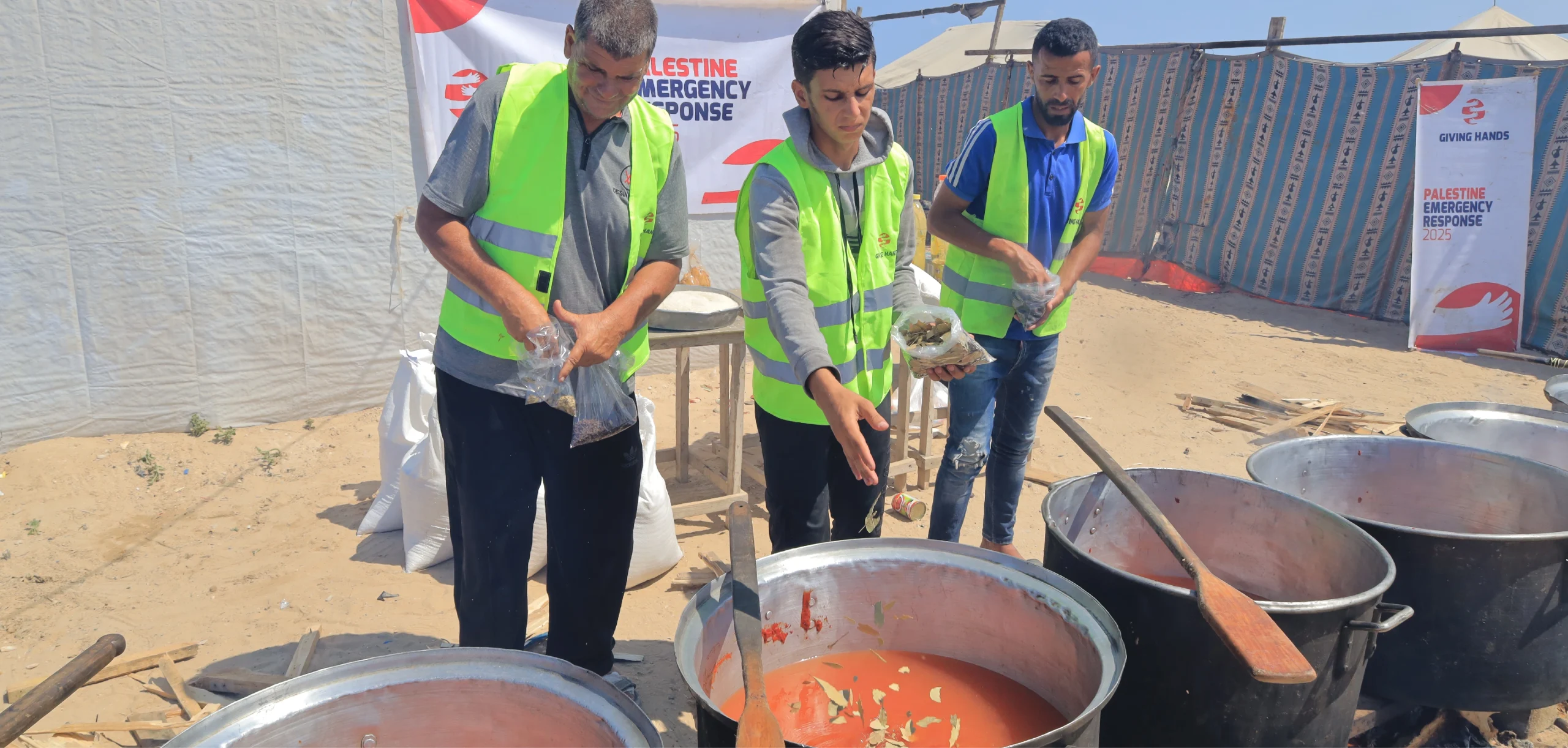 Volunteers in high-visibility vests prepare large pots of food outdoors at a Giving Hands emergency response site.