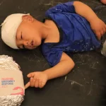 A child with a bandaged head lies on a couch next to an emergency food package labeled 