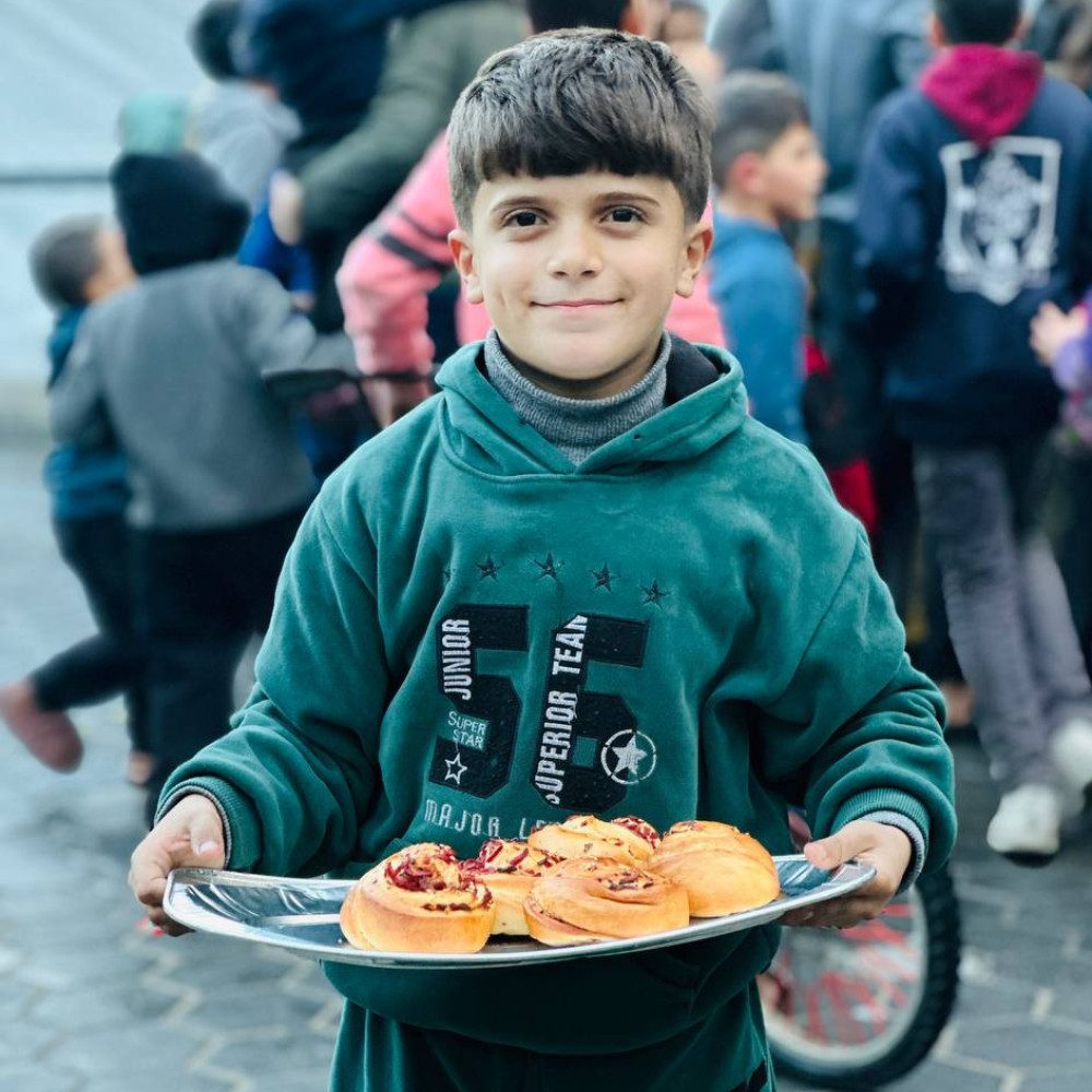 Child holding a tray of fresh pastries during a food distribution event in Palestine by Giving Hands Canada