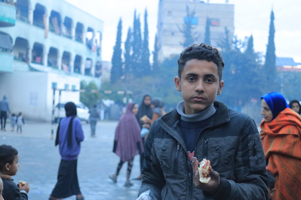 Young person holding bread in an outdoor area during a food aid distribution in Palestine by Giving Hands Canada