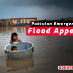 Children in a metal tub in floodwater with Pakistan Flood Appeal banner.