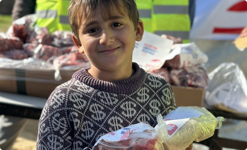 A child holds food packages received from Giving Hands at an aid distribution site.