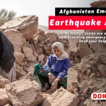Two people among earthquake rubble with Afghanistan Emergency Earthquake Appeal banner.