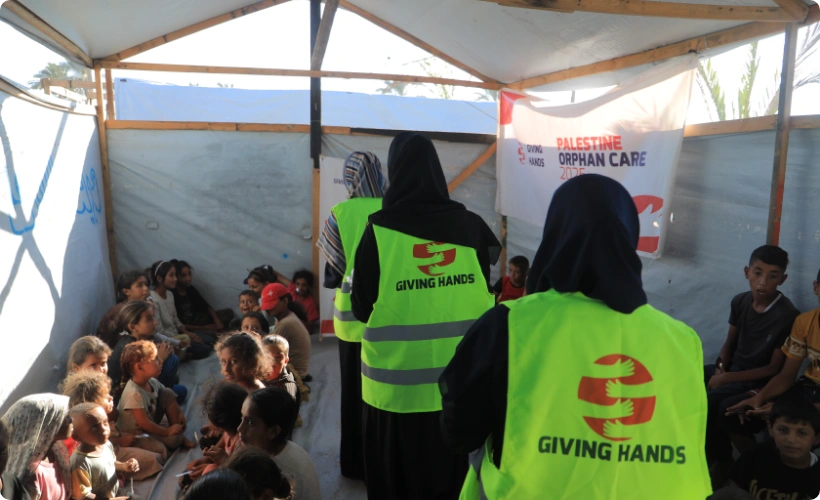 Giving Hands volunteers in safety vests leading a group activity for children at a Palestine Orphan Care event inside a shelter