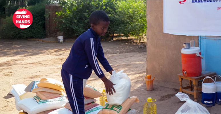 Child receiving food aid packages from Giving Hands charity during humanitarian relief distribution