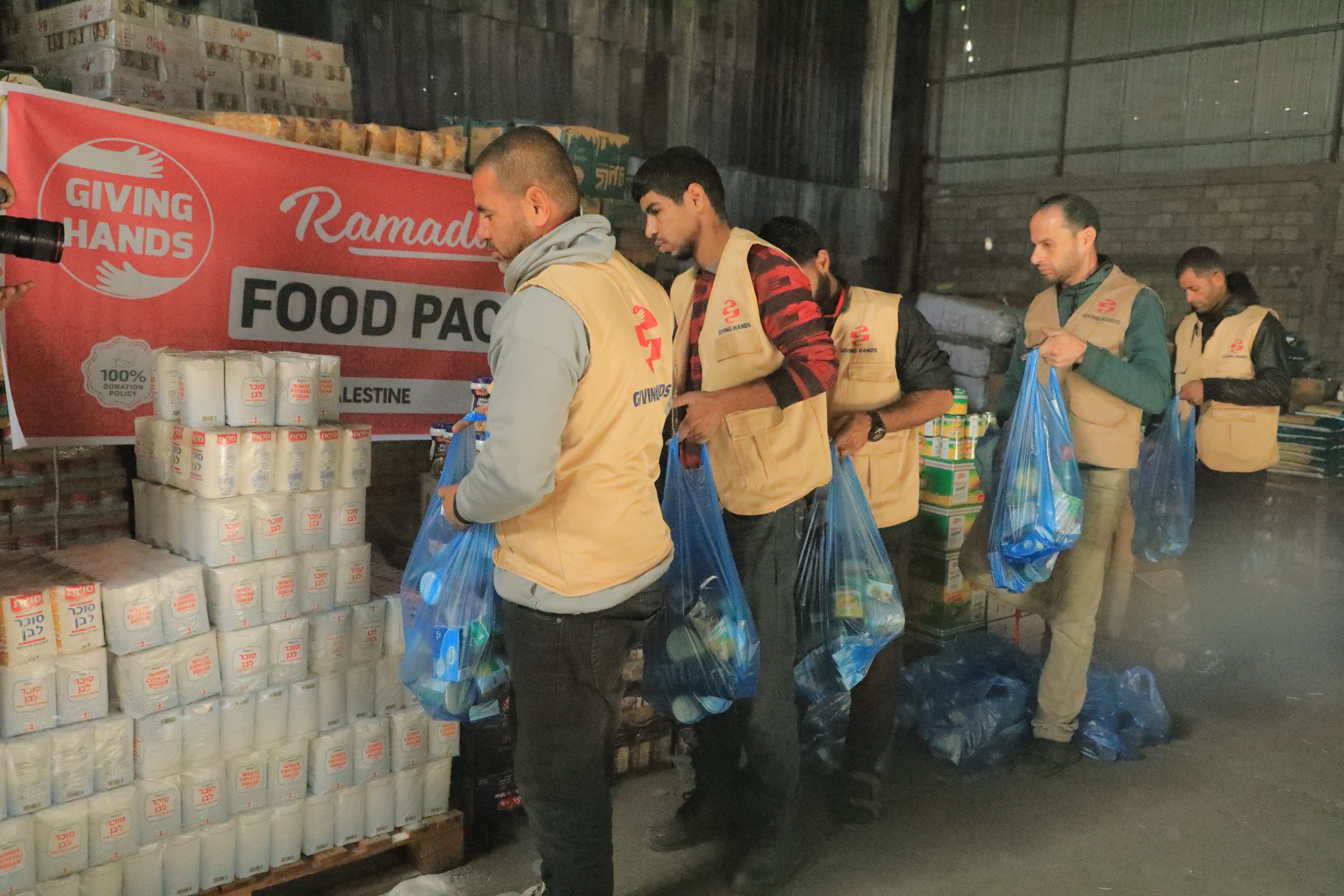 Giving Hands team preparing blue Ramadan food pack bags in a warehouse beside stacked supplies
