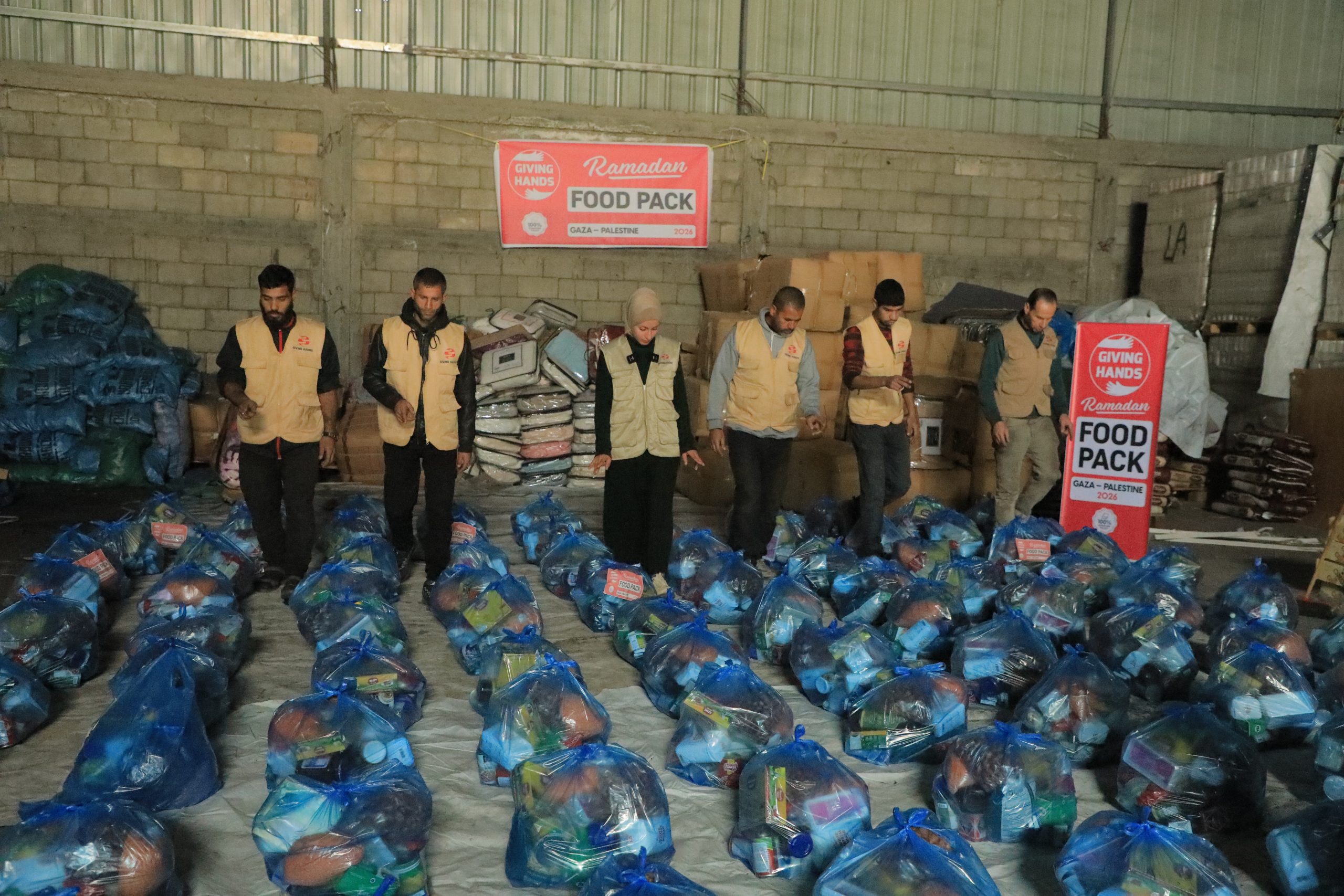 Giving Hands team standing in a warehouse surrounded by rows of packed Ramadan food parcels ready for distribution