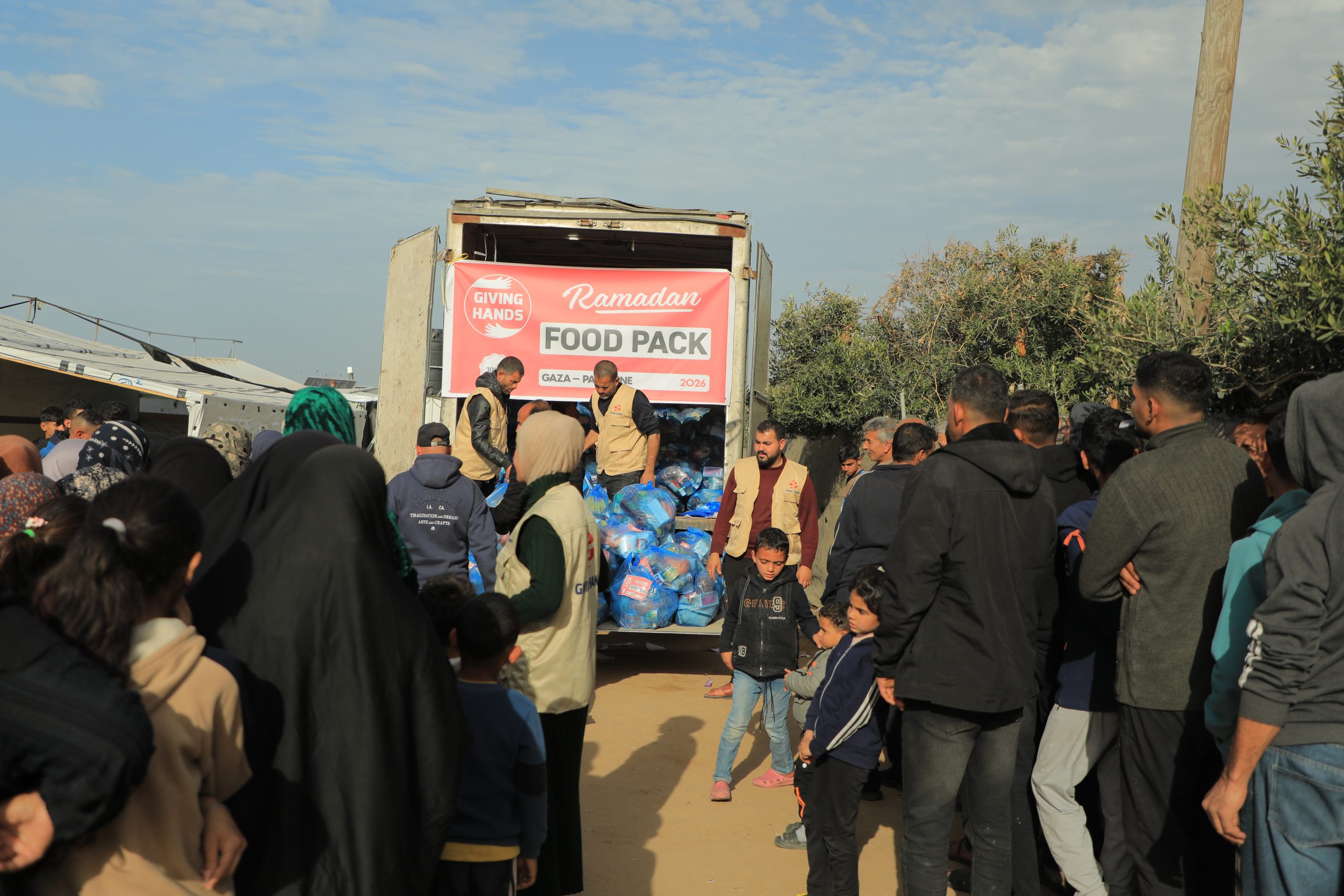 Crowd gathered around a Giving Hands truck delivering Ramadan food packs in a community