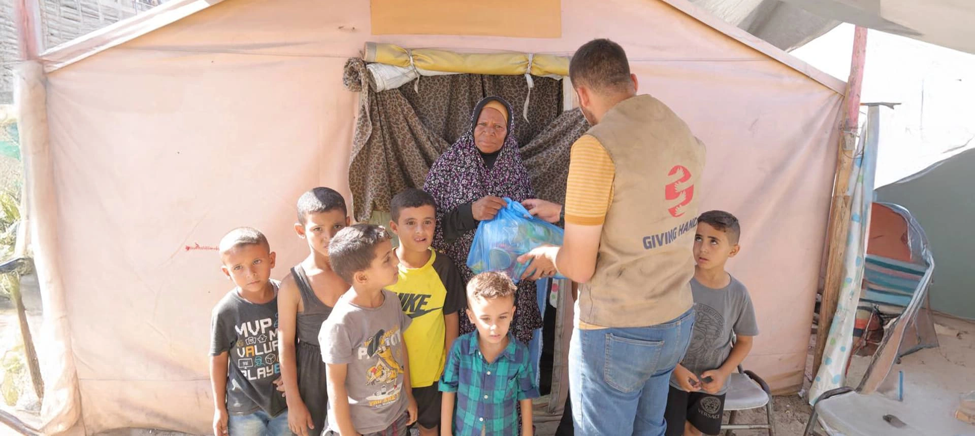 Giving Hands staff member visiting a family with several children outside a tent shelter