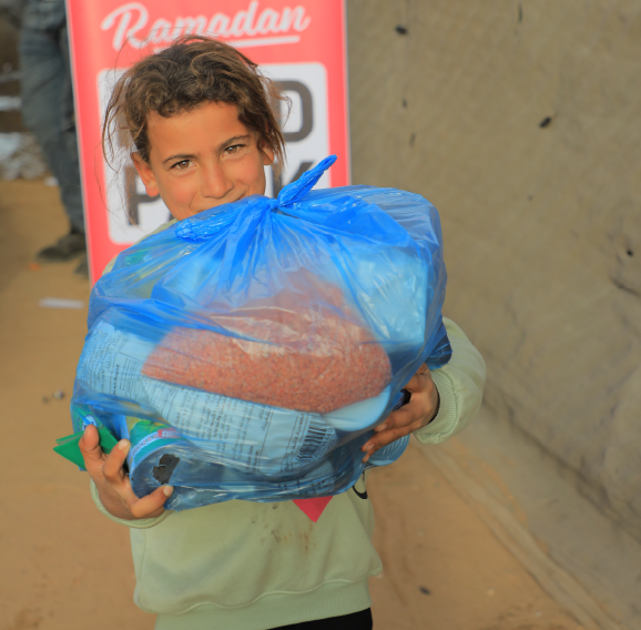 Child holding a large blue Ramadan food pack bag filled with staple supplies