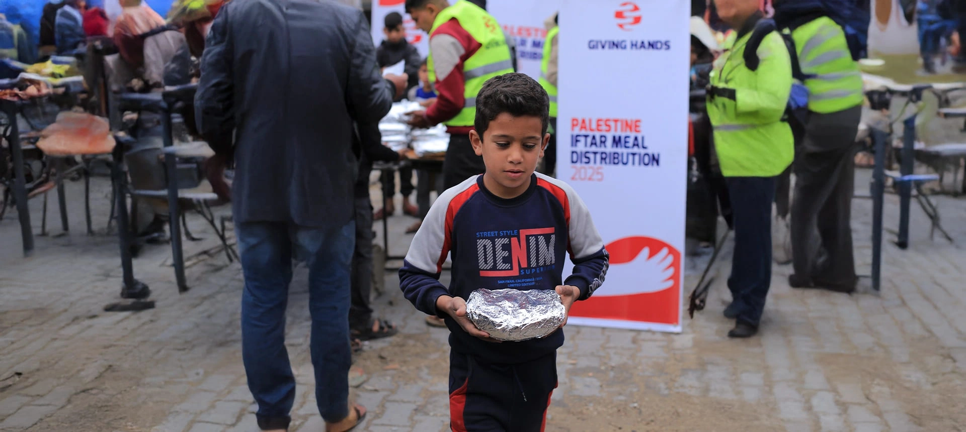 Child carrying a foil-wrapped Iftar meal at a Giving Hands distribution in Palestine